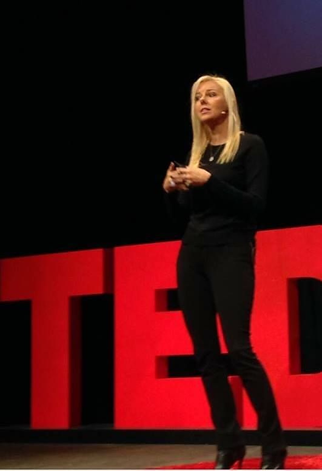 Tammy Kling speaking on the TEDx stage in front of large red TED letters.